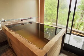 Una bañera de madera con fondo de vidrio, un grifo y una ventana con vistas a la vegetación.