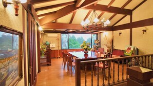 A dining area with a wooden table and chairs, a chandelier, and a view of the outdoors through large windows. - Hakone Rose Hill Private Duplex Villa (Hakone)