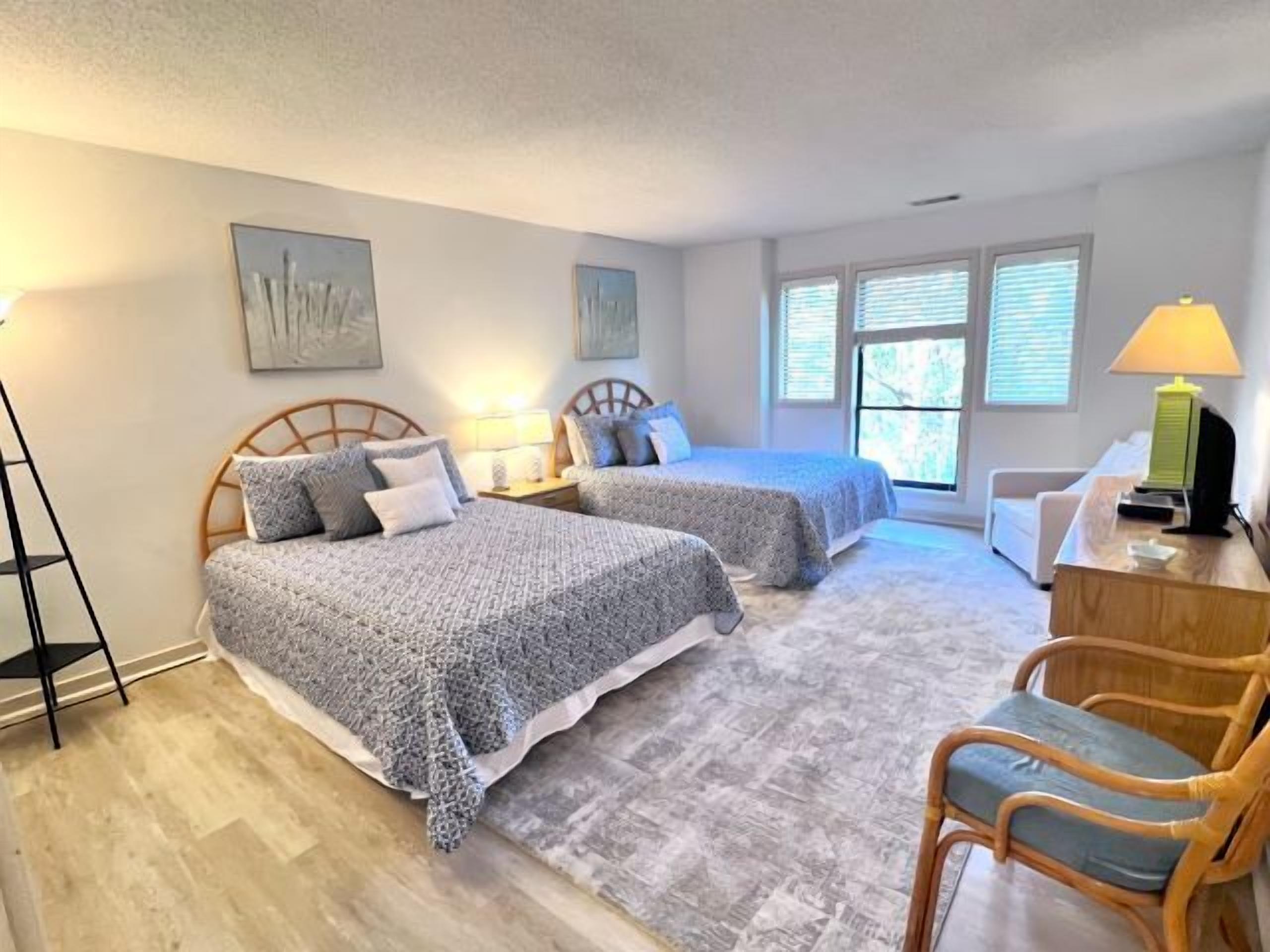 A bedroom with two beds, a desk, a chair, and a window with blinds.