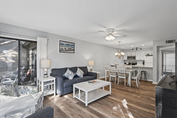 A modern living room with a grey sofa, white coffee table, and a dining area with a white table and chairs.