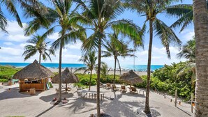 A beachside resort with thatched-roof huts, lounge chairs, and a view of the ocean.