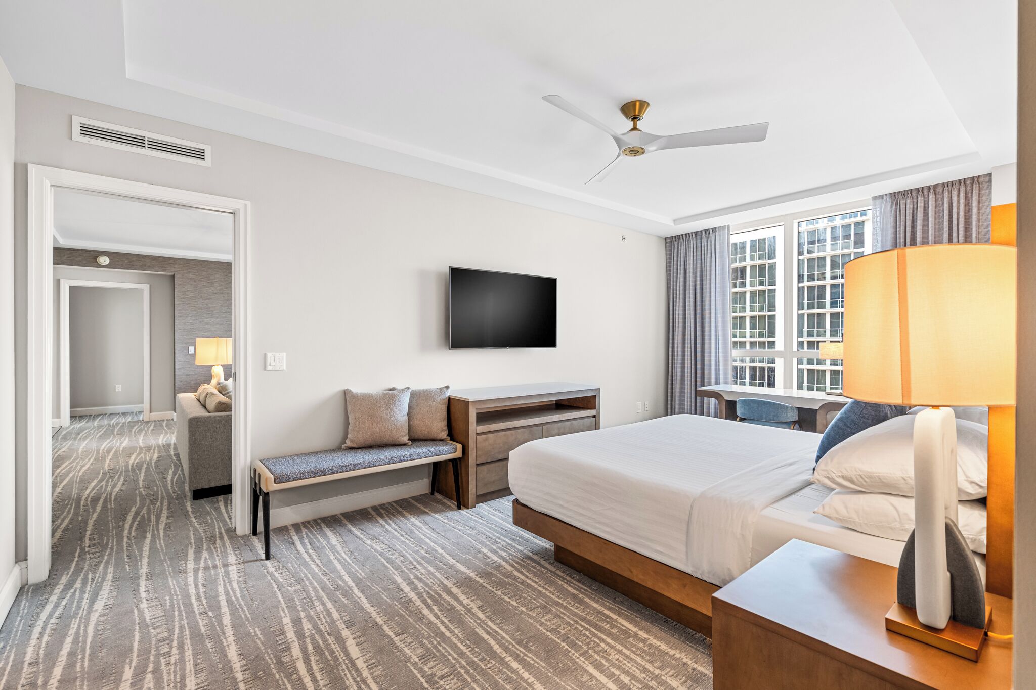 Une chambre d’hôtel avec un lit, un bureau, une télévision, un banc et une fenêtre avec des rideaux.