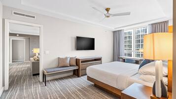 Une chambre d’hôtel avec un lit, un bureau, une télévision, un banc et une fenêtre avec des rideaux.