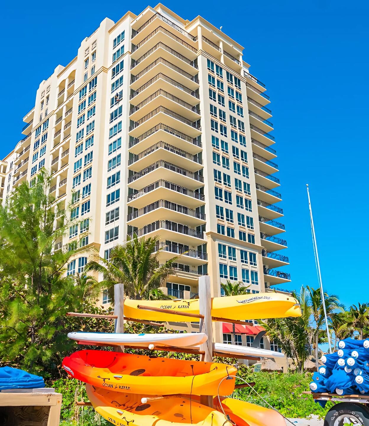 A multi-story hotel with balconies, surrounded by tropical vegetation and beach umbrellas.