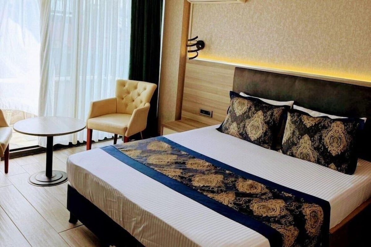 A hotel room with a bed, a round table, a chair, and a window with curtains.