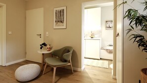 A room with a wooden floor, a green chair, a small round table, and a framed picture on the wall. - Beautiful apartment 2 in Bad Neustadt next to Rhön Klinikum Campus (Bad Neustadt an der Saale)