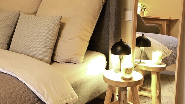 A neatly made bed with multiple pillows, a bedside table with a lamp, and a mirror reflecting part of the room. - Beautiful apartment 2 in Bad Neustadt next to Rhön Klinikum Campus (Bad Neustadt an der Saale)