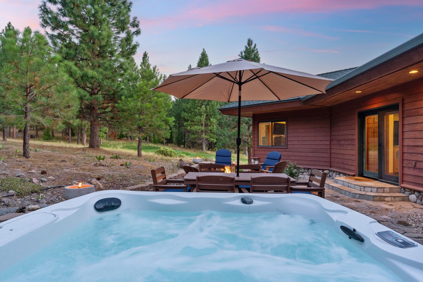 A hot tub with a wooden deck and outdoor furniture, surrounded by trees.