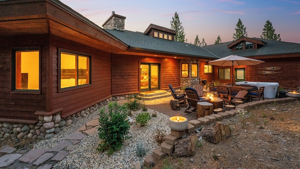 A wooden cabin with a stone foundation, a patio with outdoor seating, and a hot tub.