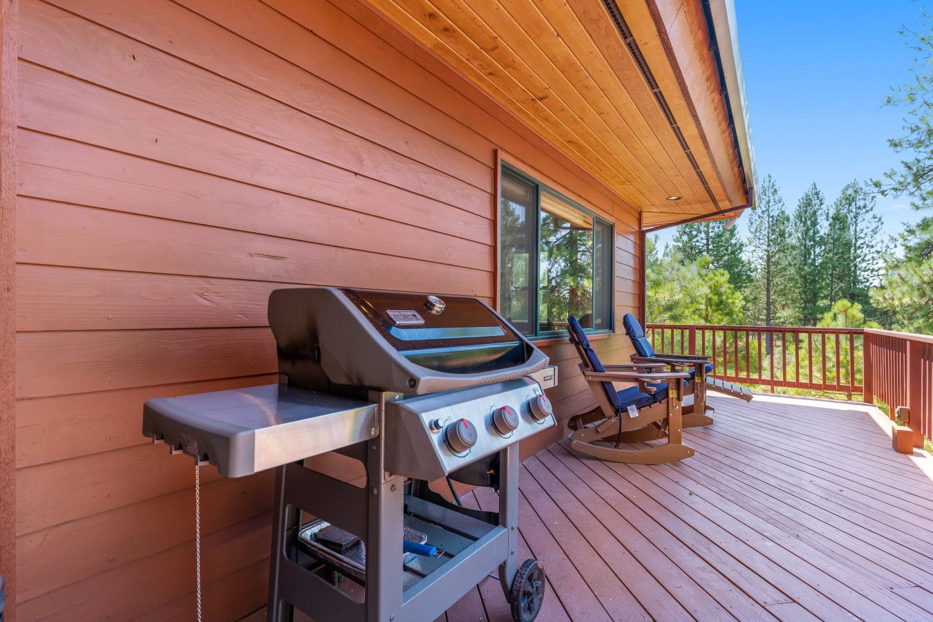 A wooden deck with a barbecue grill and two rocking chairs.