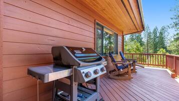 A wooden deck with a barbecue grill and two rocking chairs.