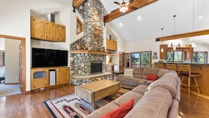 A spacious living room with a stone fireplace, wooden beams, a large TV, and a cozy seating area.