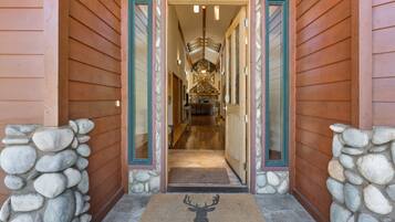 A wooden building entrance with a stone wall, a welcome mat, and a staircase leading to a room with a stone fireplace.