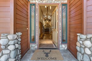A wooden building entrance with a stone wall, a welcome mat, and a staircase leading to a room with a stone fireplace. - The Luxe Lodge | Private Hot Tub | Golf | Views (Clio)