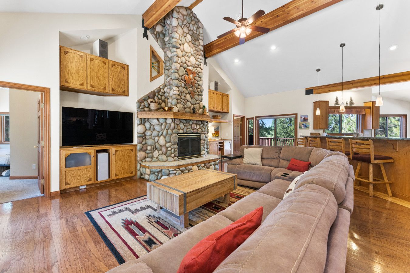A spacious living room with a stone fireplace, wooden beams, a large TV, and a cozy seating area.