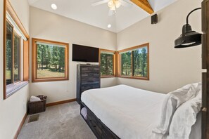 A bedroom with a large bed, a TV mounted on the wall, and a window with a forest view.