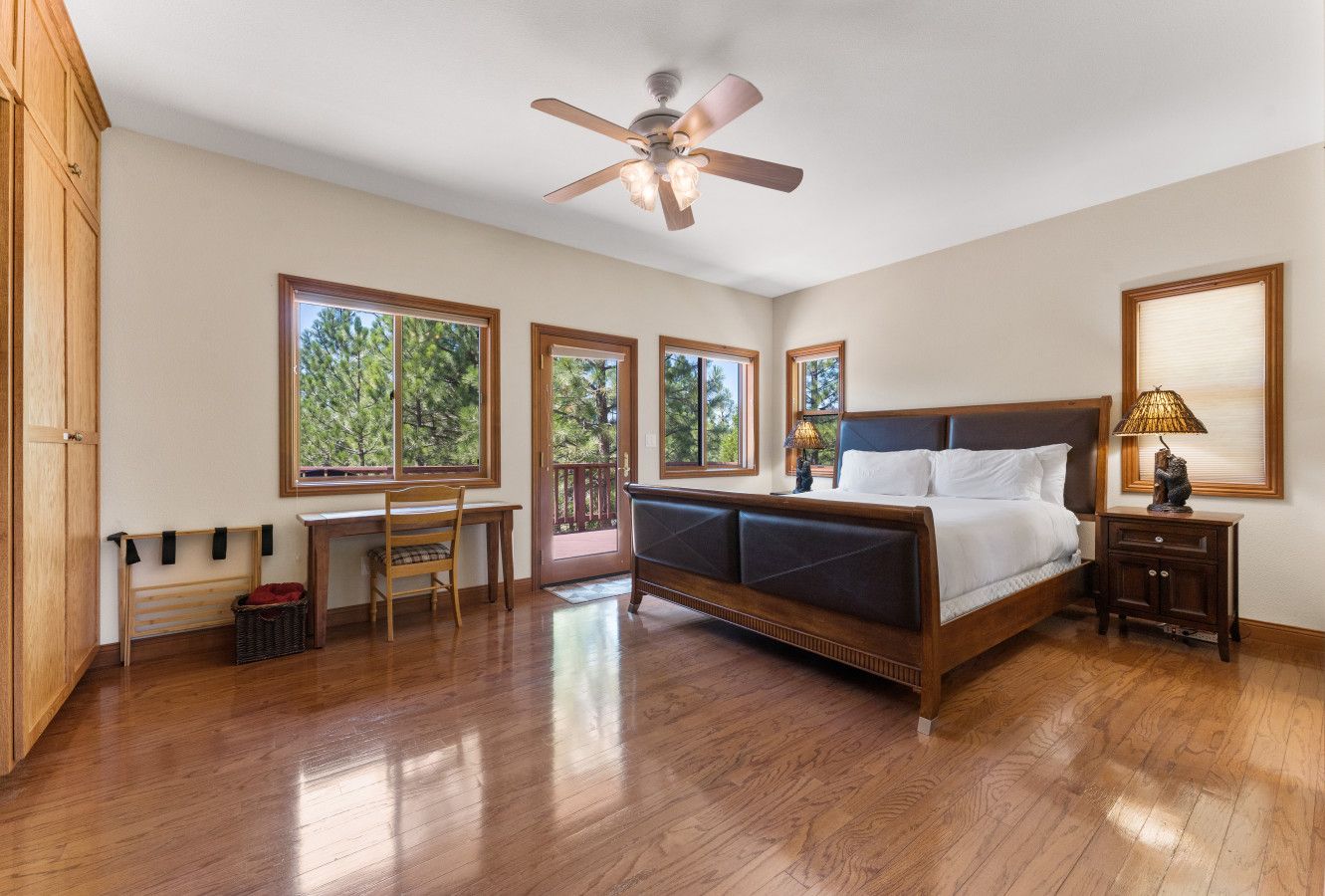 A bedroom with a wooden bed, a desk, a chair, and a ceiling fan.