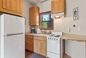 A compact kitchen with wooden cabinets, a white refrigerator, a stove, and a coffee maker.