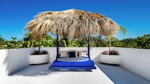 A modern outdoor seating area with a thatched roof, a circular blue cushion, and white walls. - Spacious Villa w/ Private Pool – Ideal for Groups, Steps to Tamarindo Beach (Tamarindo)