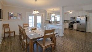 Et moderne køkken med hvide skabe, rustfrie stålemmer og et spiseområde med træstole og et bord.