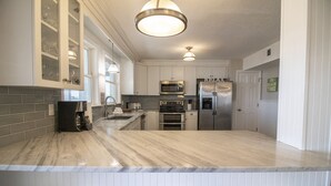Et moderne køkken med marmor bordplader, rustfrie stål hvidevarer og en central ø.