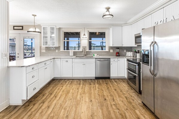 A modern kitchen with white cabinetry, stainless steel appliances, and a wooden floor.