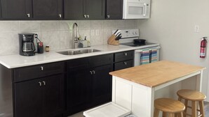 A kitchen with dark cabinets, a white countertop, a microwave, a coffee maker, and a trash bin. - Waterfront Retreat with Kayaks (Inverness)