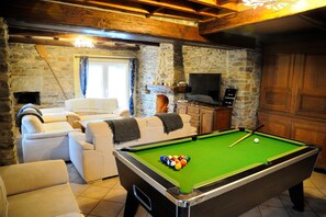 Une table de billard avec des billes, un canapé, un téléviseur et des murs en pierre.
