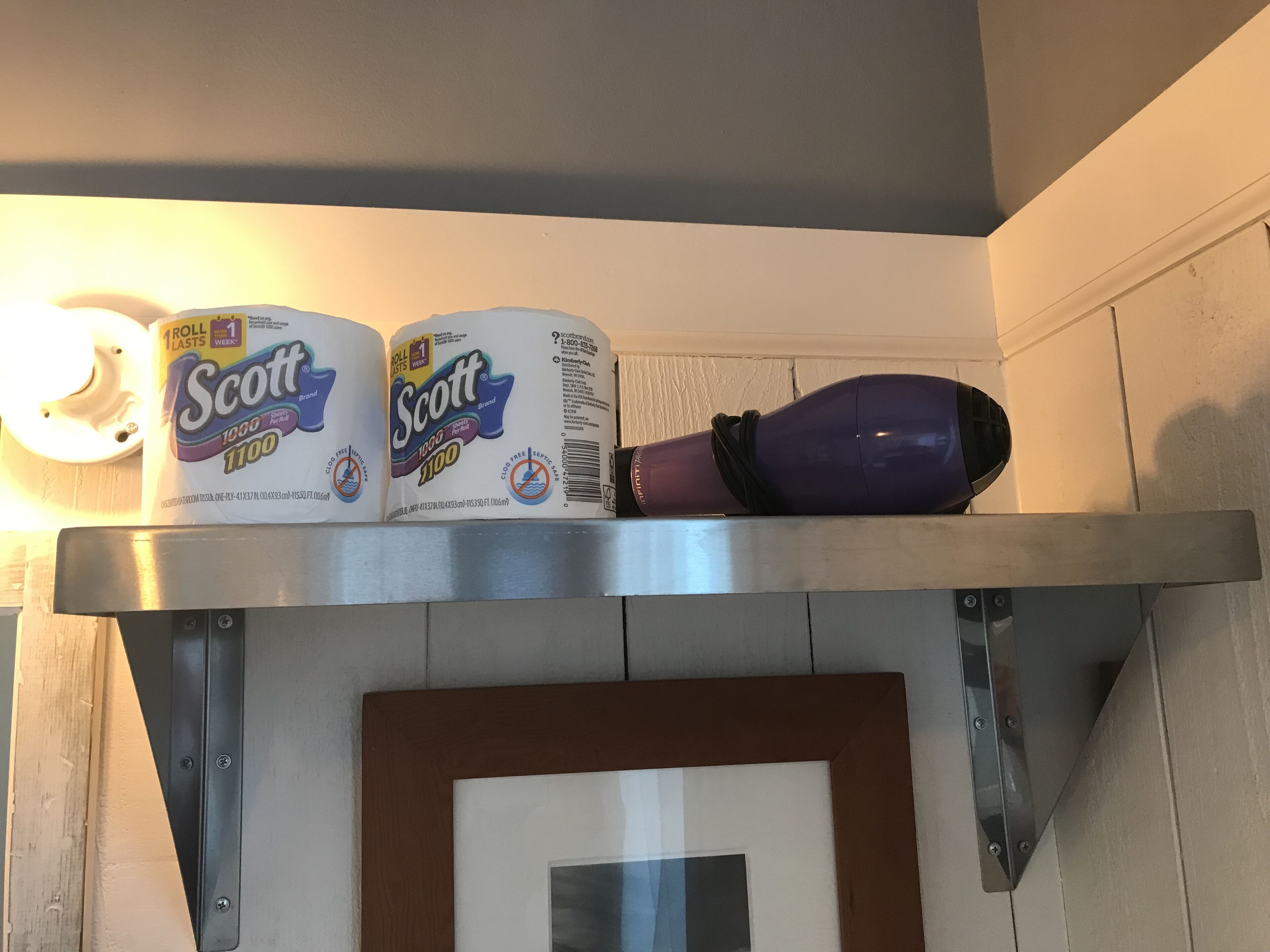 A shelf with two Scott 1000 rolls of toilet paper and a purple water bottle.