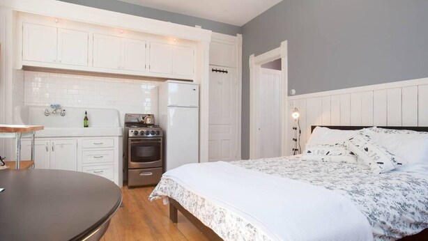 Une chambre comprenant un lit, une table de chevet, une commode et un coin cuisine intégré avec un réfrigérateur, un four et un évier.