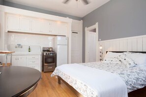 A bedroom with a bed, a nightstand, a dresser, and a built-in kitchen area with a refrigerator, oven, and sink. - iKlektik House // Robin (Chicago)