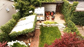 Un jardin avec un espace barbecue, une terrasse couverte et un mur en pierre.