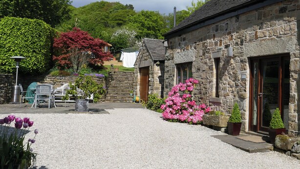 A stone building with a gravel courtyard, a wooden door, and a small garden with pink flowers. - 2 bedroom accommodation in Bakewell (Bakewell)