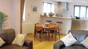 A living room with a brown leather sofa, a dining table with chairs, and a kitchen area in the background. - 2 bedroom accommodation in Bakewell (Bakewell)