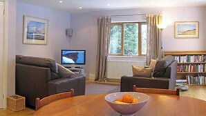 A living room with two sofas, a TV, a bookshelf, and a window with curtains. - 2 bedroom accommodation in Bakewell (Bakewell)