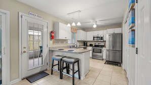 Una cocina con una isla central, armarios blancos, electrodomésticos de acero inoxidable e iluminación colgante.