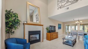 Una sala de estar con chimenea, sofá azul, mueble de entretenimiento de madera y un comedor con sillas y mesa.