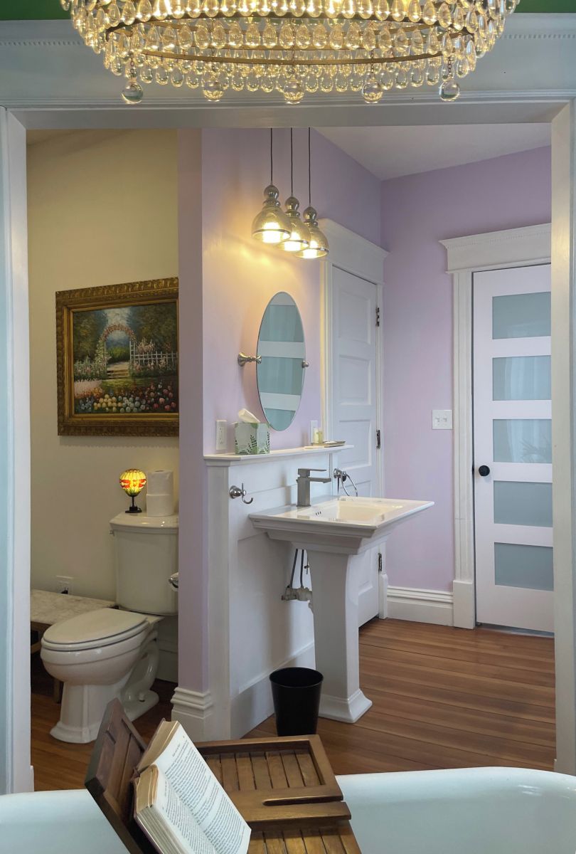 A bathroom with a white vanity, a mirror, a chandelier, and a painting on the wall.