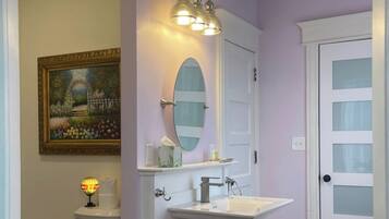 A bathroom with a white vanity, a mirror, a chandelier, and a painting on the wall.