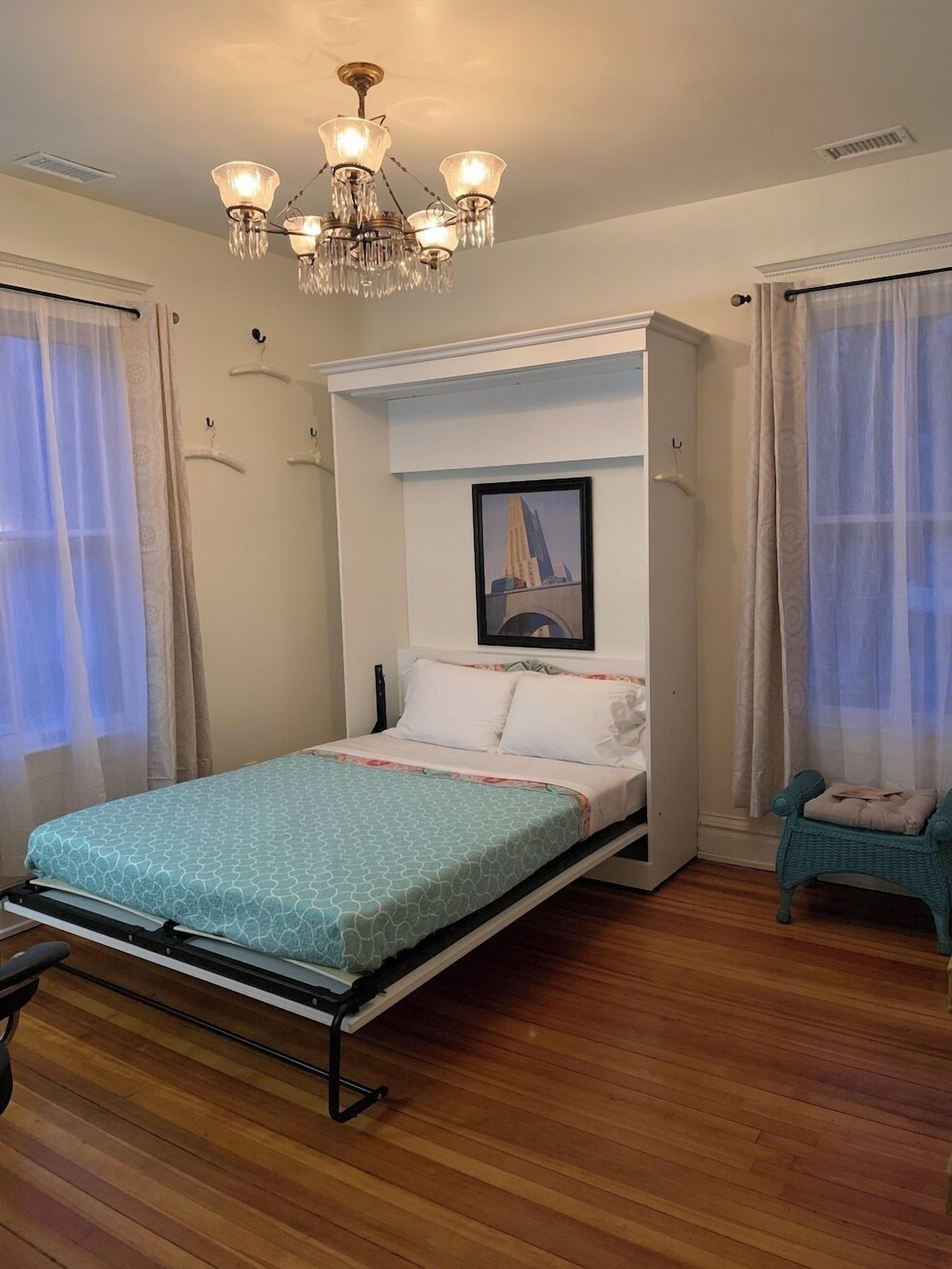 Een kleine slaapkamer met een bed, een kroonluchter, een ingelijst beeld aan de muur en een stoel.