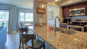 A kitchen with granite countertops, stainless steel appliances, and a dining area with bar stools.