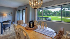 A dining area with a wooden table, chairs, a woven centerpiece, and a view of a green landscape through large windows.