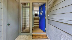 A front door with a blue doorbell, a welcome mat, and a staircase leading to an upper level.