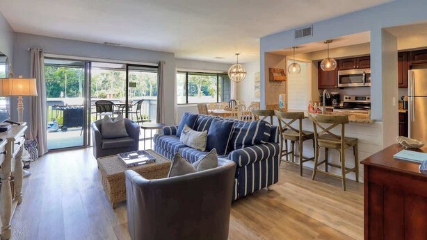 A modern living room with a sofa, armchairs, a dining table, and a kitchen area with cabinets and appliances.