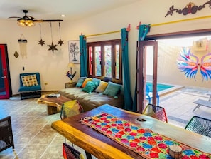 A cozy living room with a sofa, coffee table, and chairs. There is a pool visible through the glass doors.