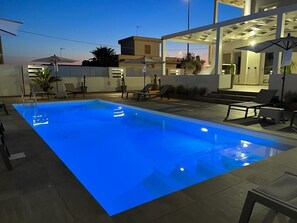 A swimming pool with a blue light, lounge chairs, umbrellas, and a modern building in the background. - Elite Luxury Residence (Racale)