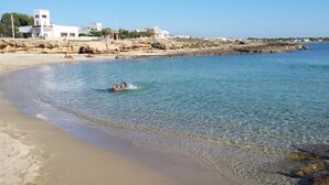 Una playa con agua cristalina, una orilla arenosa y edificios al fondo.