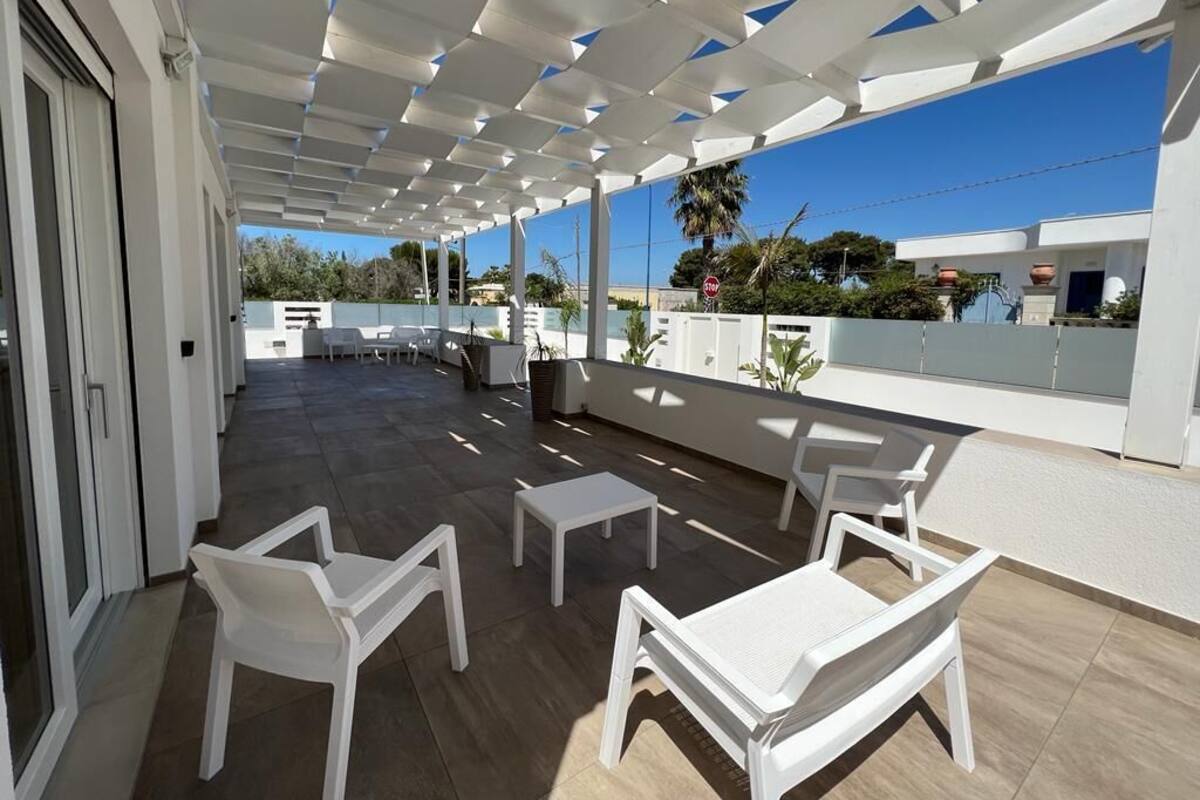 An outdoor patio with white furniture, a pergola, and a view of the surrounding area.