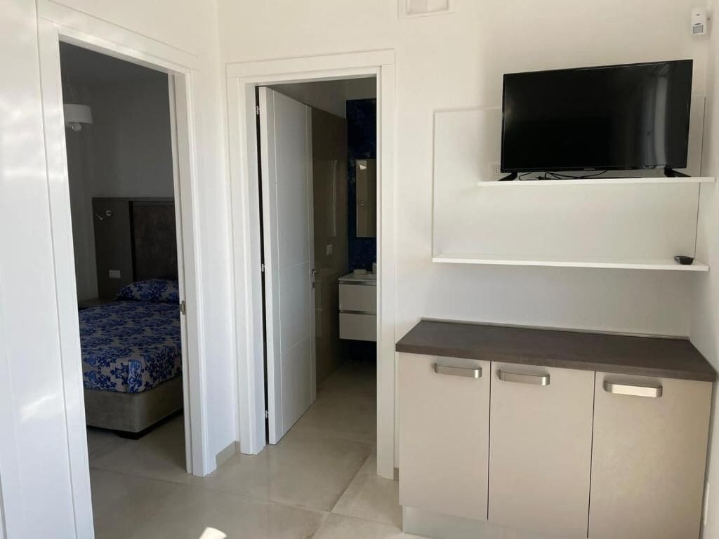 Ein Schlafzimmer mit einem Bett, einem an der Wand montierten Fernseher und einem Schrank mit Schubladen.