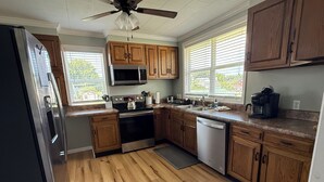 Cucina con mobili in legno, elettrodomestici in acciaio inossidabile, una ventola a soffitto e ampie finestre.